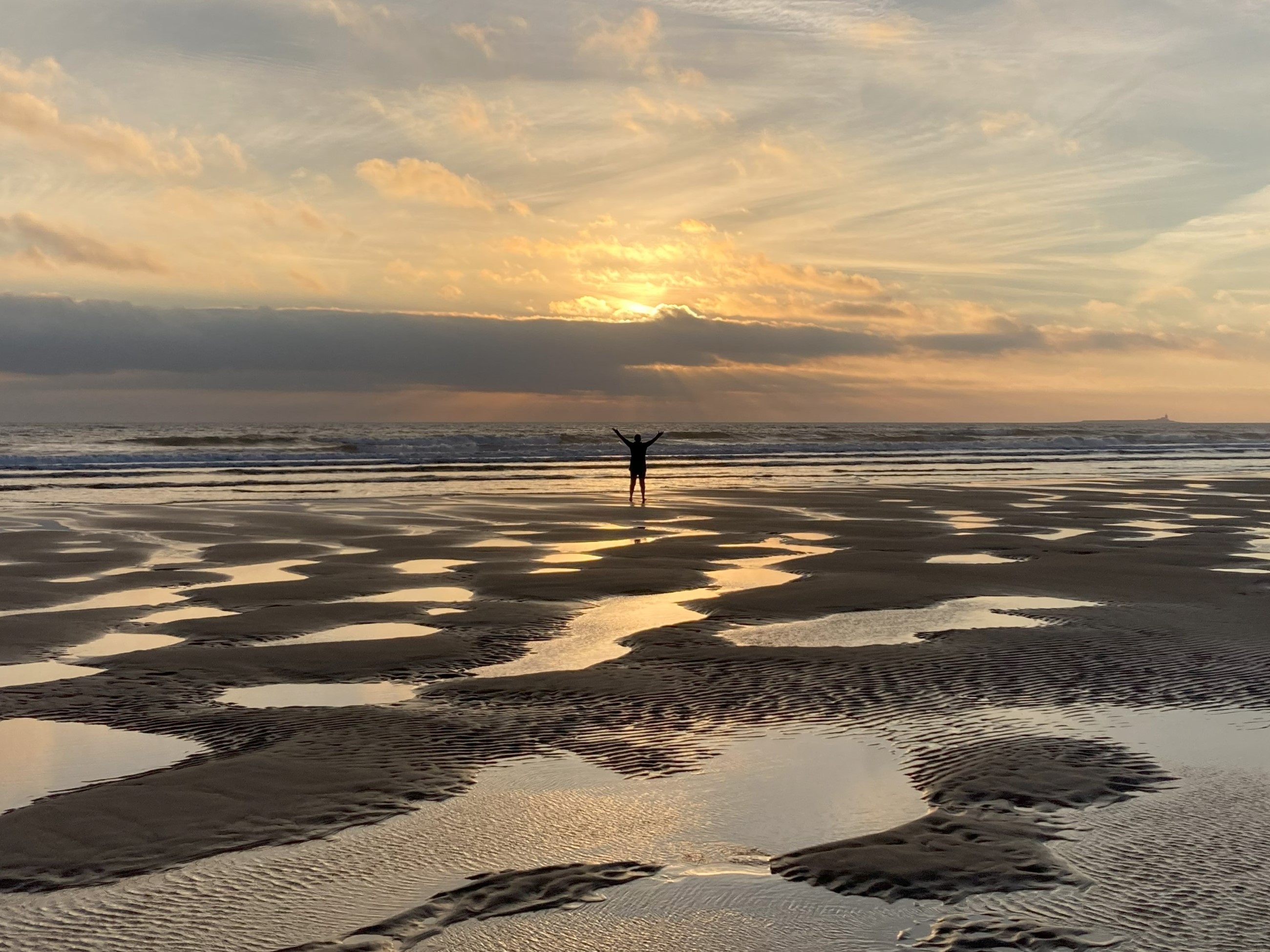 Winter Sun Rise at Alnmouth beach. A lone figure raises their arms in awe to the sea and sun.